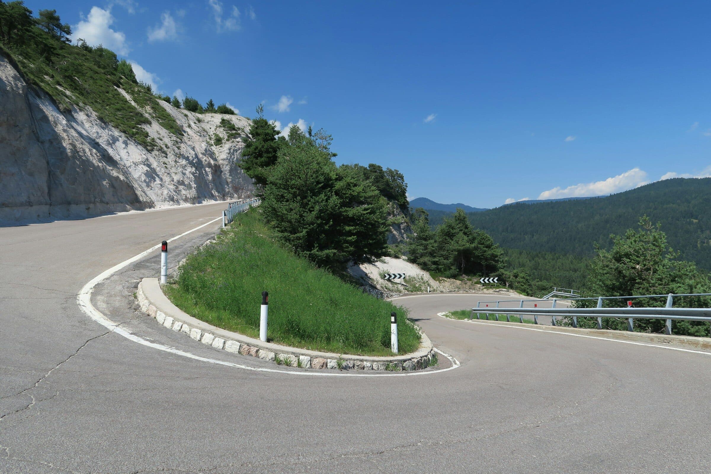 Un tornante su una strada di montagna, visto dall'alto: la strada svolta e sparisce tra gli alberi.